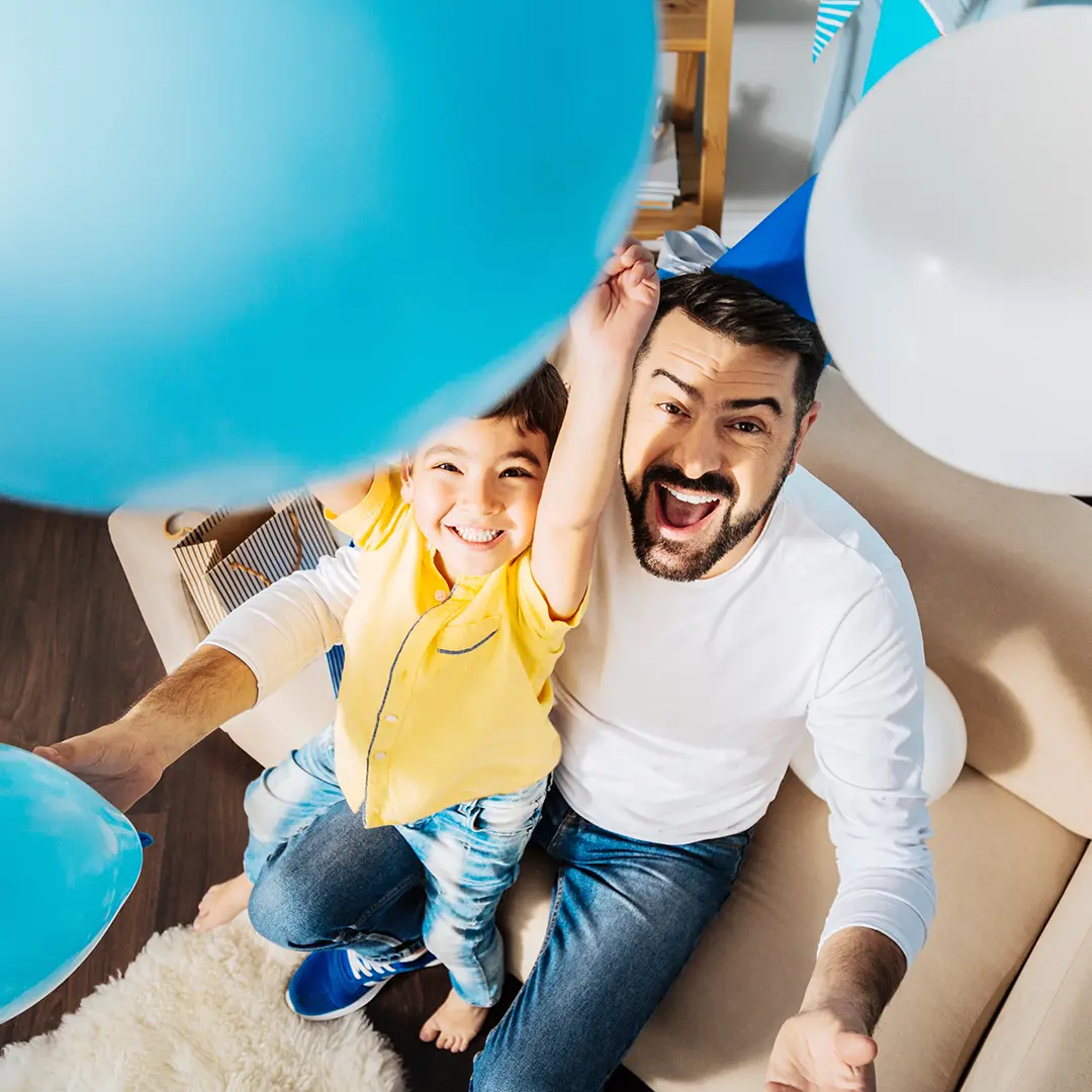 Pappa och son leker med ballonger i vardagsrummet – enkla barnkalas lekar som passar perfekt hemma.