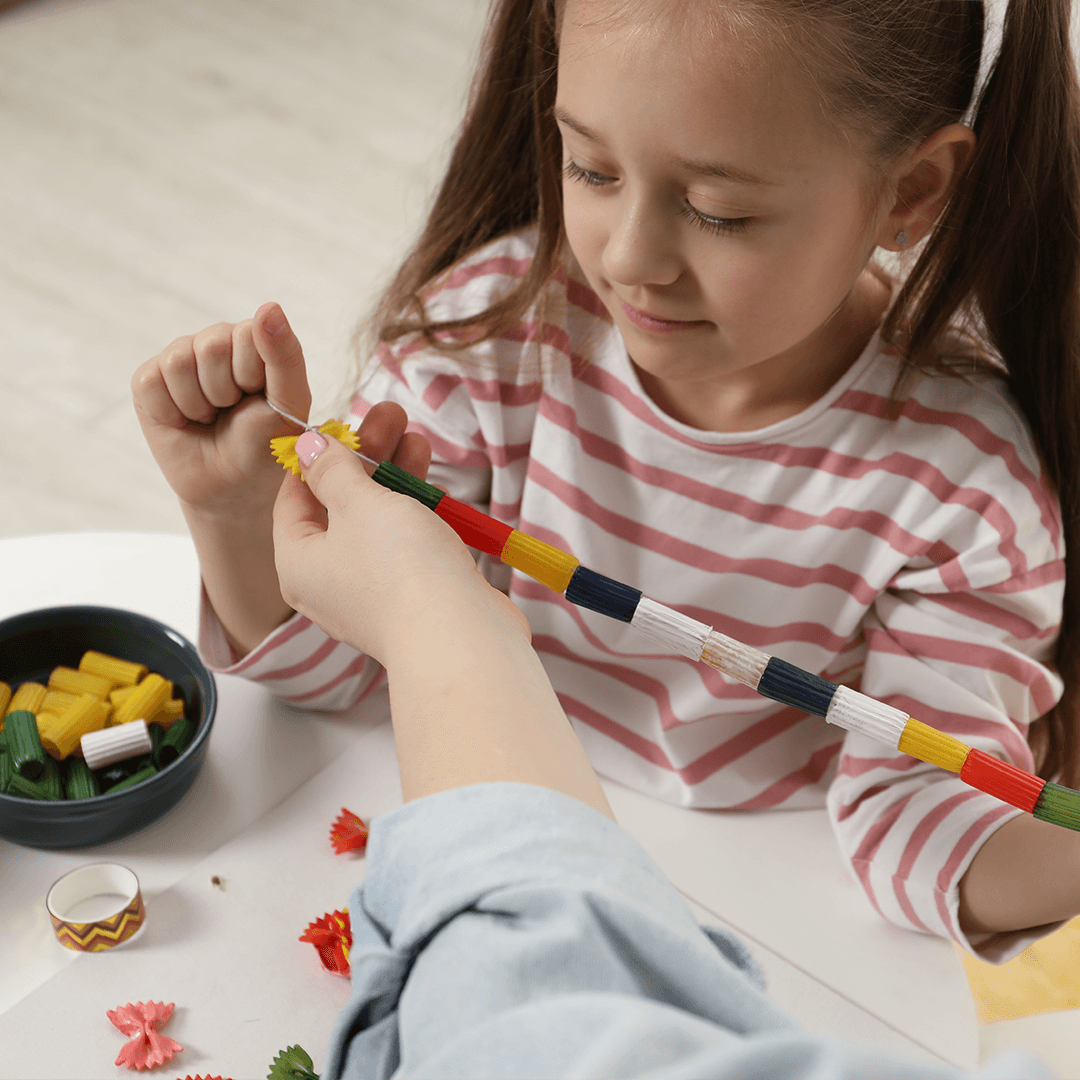 Flicka gör pastahalsband med sin mamma – roliga aktiviteter barn gillar hemma.