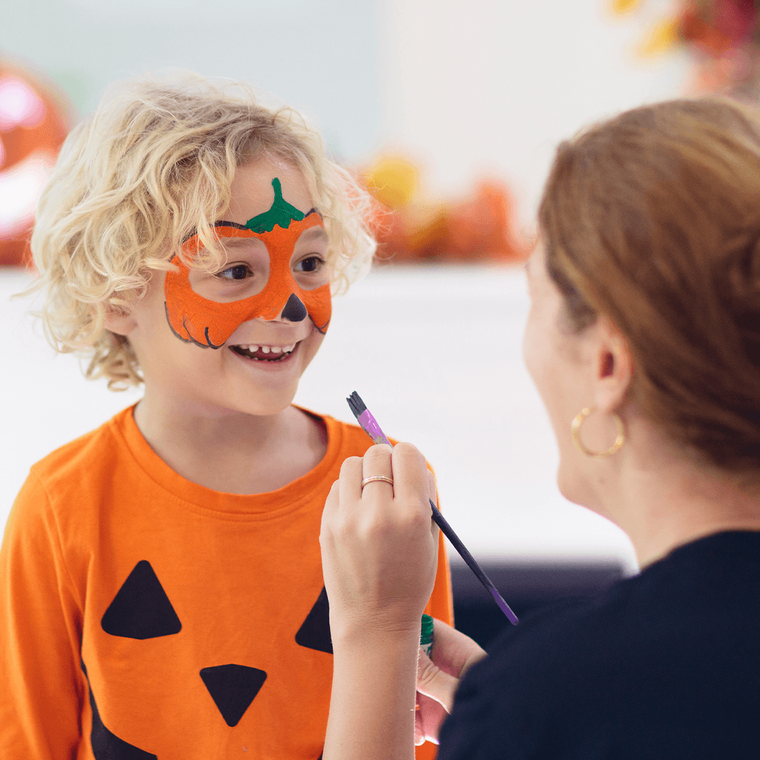 Mother paints a pumpkin face design on her son for Halloween