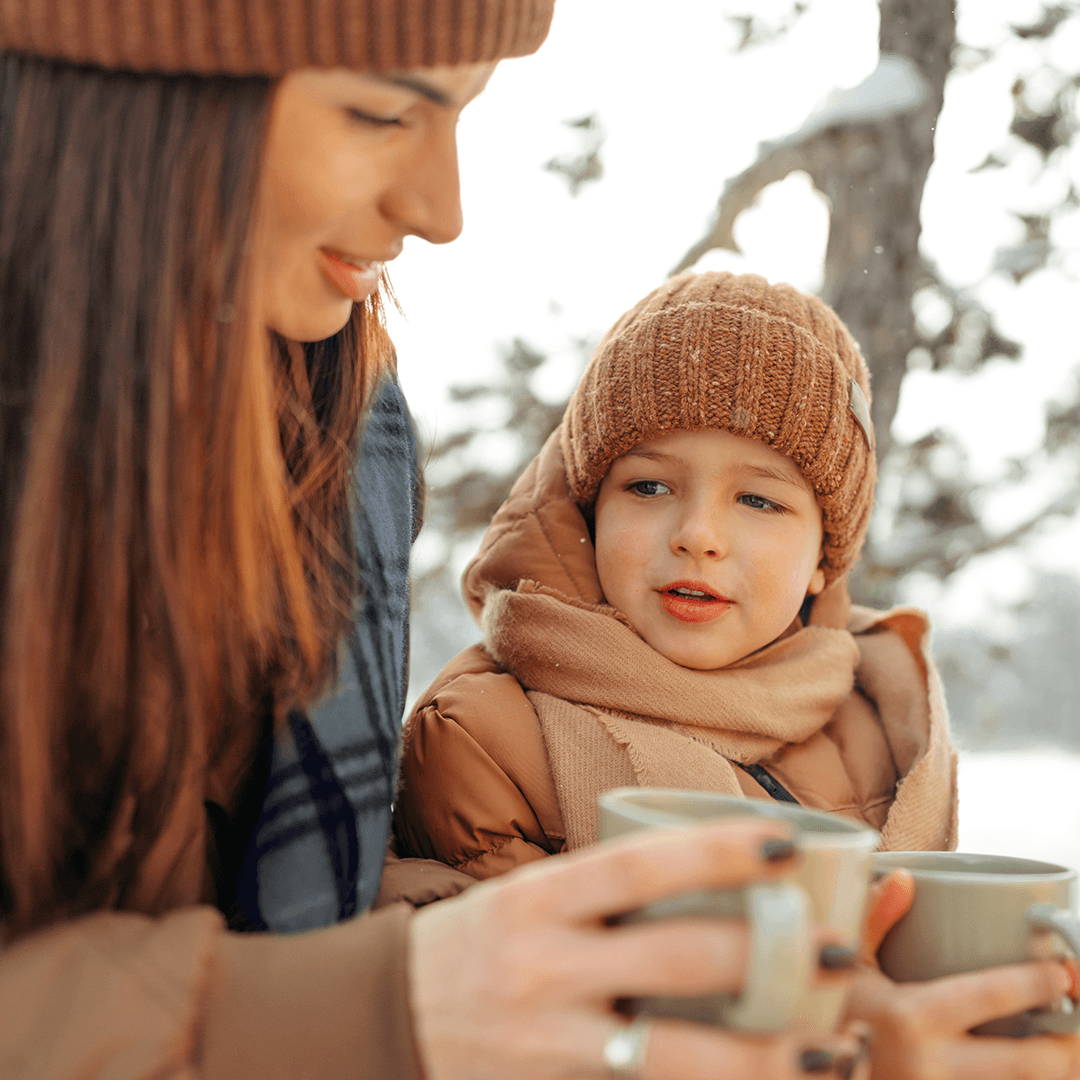 Mother and child eating snacks outdoors in winter.